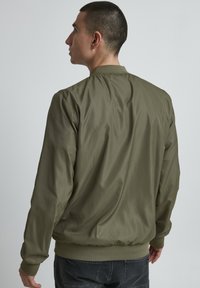 Olivgrüne Bomberjacke mit glatter Oberfläche, gerippten Bündchen und Kragen. Sie hat eine lockere Passform und keine auffälligen Details.
