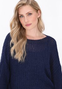Dunkelblau gestrickter Pullover mit weitem Halsausschnitt und langen Ärmeln; offene Struktur und lockere Passform. Subtiler Entwurf ohne Muster oder Akzente.