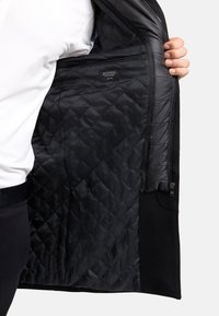 Sort, kviltet jakke indvendig med en glat tekstur og detaljeret syning. Har en lynlås og et mærke indeni. Yderstoffet fremstår robust.