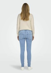 Svijetloplave skinny traperice s srednjim strukom, koje imaju dva stražnja džepa i čist, besprijekoran dizajn. Ušivene su s krem puloverom i bijelim tenisicama.