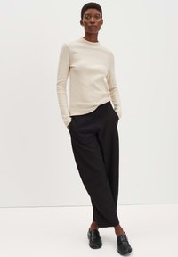 Beige Langarmoberteil aus weichem Stoff, kombiniert mit lockeren schwarzen Hosen, die ein glattes, minimalistisches Design aufweisen, und eleganten schwarzen Schuhen.