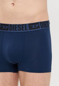 Boxer briefs bleu marine avec une texture lisse et le logo Diesel sur la ceinture élastique, présentant une coupe ajustée et une longueur mi-cuisse.