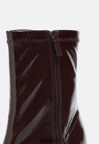 Lesklé burgundské kotníkové boty se zipem, s hladkou texturou a úzkým siluetou. Prošívané detaily podél švů.