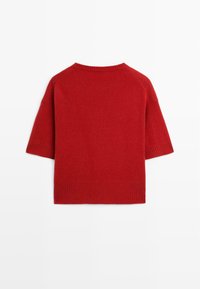 Maglione rosso a maglia con collo rotondo, maniche raglan corte e orlo a coste. Texture morbida, design minimale e colore uniforme.