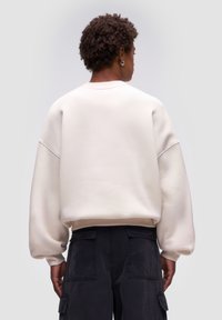Sweatshirt oversized color crema con spalle ribassate, polsini a coste e una finitura testurizzata, abbinato a pantaloni cargo scuri con tasche laterali.