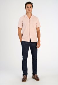 Koszula z krótkim rękawem w jasnoróżowym kolorze z białymi paskami, zestawiona z granatowymi spodniami i brązowymi butami żeglarskimi. Prosty kołnierz.