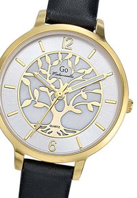 Montre dorée avec un motif d'arbre sur un fond argenté, accompagnée d'un bracelet en cuir noir. Mouvements à quartz indiqués en bas.