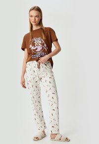 Bruine katoen t-shirt met een "Cowgirl" grafiek en korte mouwen, gecombineerd met witte, gestreepte pyjamabroek met cowboote en sterren.