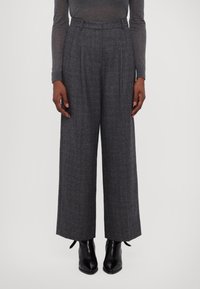 Grau karierte weit geschnittene Hose mit hoher Taille, ausgestattet mit Falten und einem strukturierten Stoff, kombiniert mit schwarzen Knöchelstiefeln.