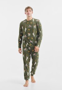 Zelený pyžamový set s dlouhým rukávem, který obsahuje hravé ilustrace psů a potravin. Měkká látka s žebrovanými manžetami a elastickým pasem.