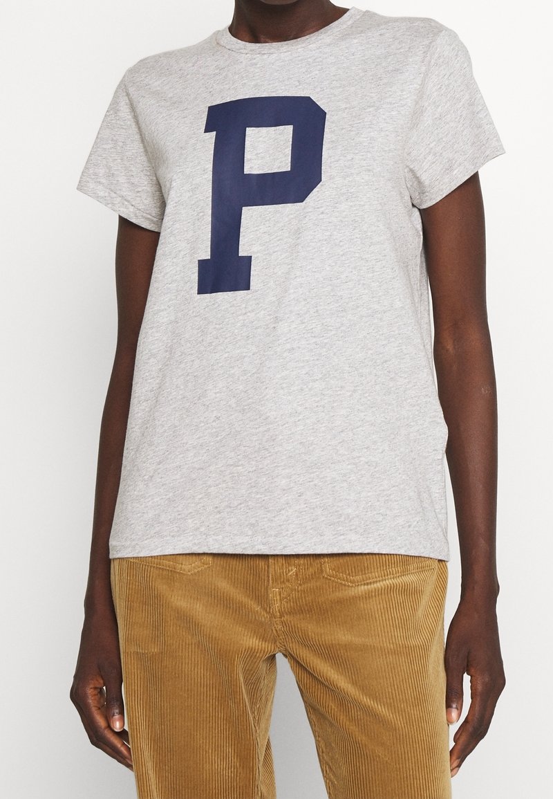 Grå bomulls t-shirt med en stor marinblå "P" grafik. Korta ärmar, rundad halsringning, avslappnad passform. I kombination med beiga kordbyxor.