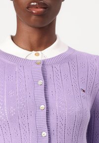 Cárdigan de punto lila con un delicado patrón de calados, que presenta un cuello blanco, un cierre de cinco botones y un pequeño acento de logo.