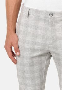 Light gray trousers made of textured fabric. Features a check pattern and a single button at the waist. Side pocket visible.