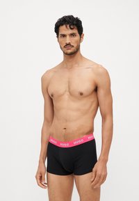 Schwarze Boxershorts mit einem pinken, markierten Bund. Der Stoff sieht glatt aus, hat eine figurbetonte Form und minimale Nähte.