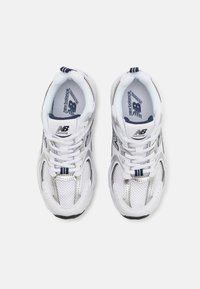 Baskets de sport blanches avec une tige en mesh et en synthétique, présentant des accents bleu marine, des détails réfléchissants et un col rembourré pour le confort.