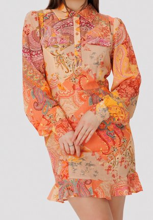 Robe avec un col chemise, des manches longues et un ourlet à volants. Présente un motif paisley orange avec des accents floraux sur un fond clair.