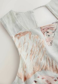 Gros plan d'une robe sans manches en lin de couleur claire avec des motifs abstraits de papillons et d'ailes en rose doux et beige.