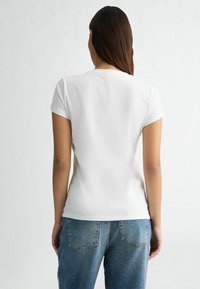 T-shirt bianca a maniche corte con taglio classico, texture morbida e design semplice, abbinata a jeans in denim blu con tasche posteriori.