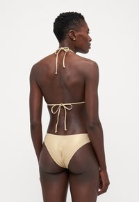 Beige bikini sett med halterneck-top med knytefeste og matchende lave truser, laget av glatt, blankt materiale.