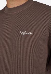 Brun ribbet sweater med rund hals og hvid broderet "Pegador" logo på venstre bryst. Blød tekstur og tætsiddende design.