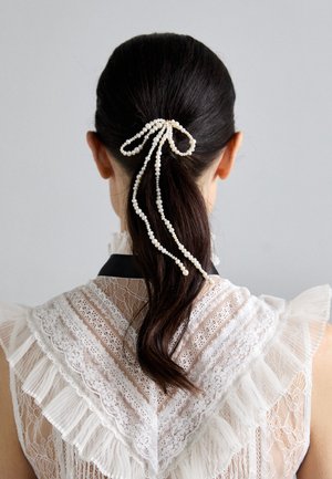 Hair accessory with pearl strands in a bow shape, featuring delicate texture, ivory color, attached to a dark ponytail, against a gray background.