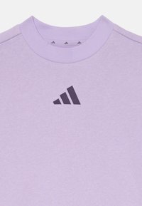 Gaiši violets džemperis ar apaļu kaklu un tumšu logotipu, kas attēlo trīs diagonālas līnijas priekšpusē.
