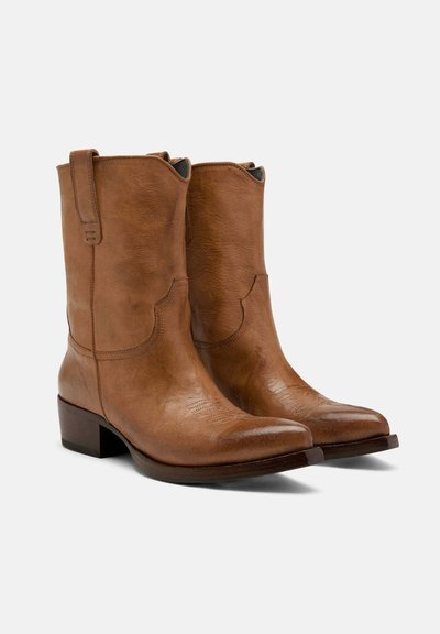 Bottes de cowboy en cuir marron avec un bout arrondi, des détails de couture subtils et un talon carré. Équipées de languettes sur les côtés pour un enfilage facile.