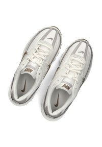White and gray sneakers featuring a mesh upper, textured accents, laces, and a prominent brown Nike logo on the sides and tongue.