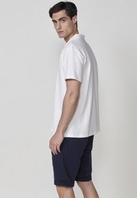 Vit kortärmad pikétröja i texturerad tyg, kombinerad med marinblå shorts med rullade avslut. Enkelt och rent design.