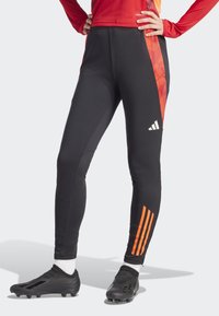 Leggings de sport noirs avec un motif géométrique rouge sur le côté, arborant trois bandes orange sur le bas de la jambe et un logo Adidas.