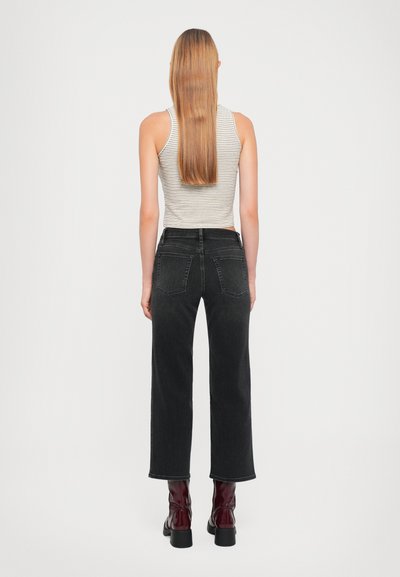 Black denim straight-leg jeans with a mid-rise waist, featuring two back pockets and minimal stitching detail, paired with glossy red ankle boots.