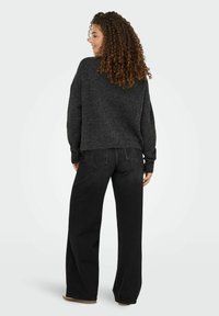 Pull en maille gris foncé ample avec un col rond, des épaules tombantes et des bords côtelés, associé à un jean noir taille haute.