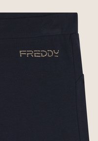 Pantaloni stretch blu navy con una texture liscia, caratterizzati dal nome "FREDDY" in strass metallici sull'anca, esposto in modo prominente.