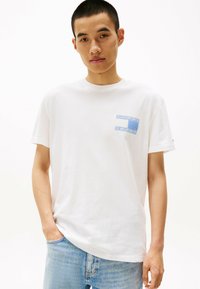 Hvid bomulds t-shirt med et blåt mønstrede lomme-design. Korte ærmer, rund hals og en afslappet pasform, parret med lyse denimjeans.