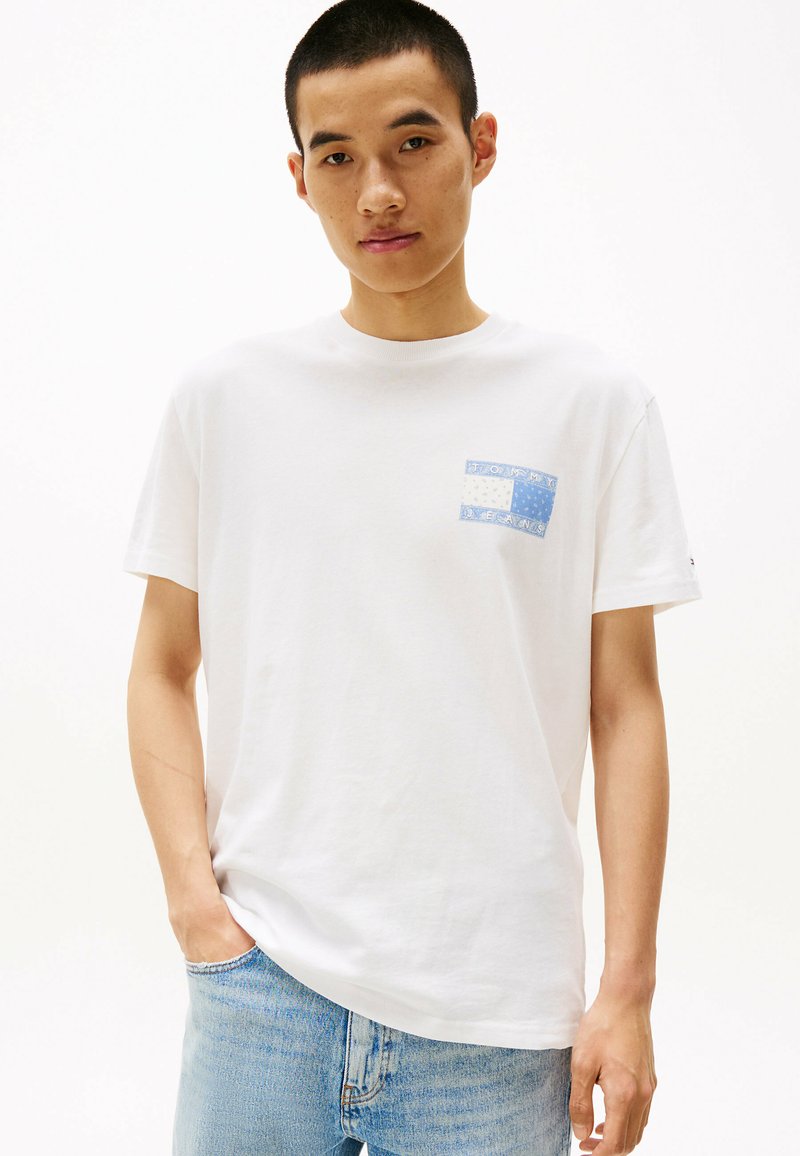Hvid bomulds t-shirt med et blåt mønstrede lomme-design. Korte ærmer, rund hals og en afslappet pasform, parret med lyse denimjeans.