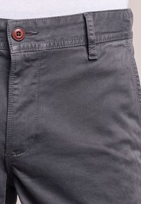 Grå bomullsblandade byxor med en slät yta, som har en brun knappstängning och sidofickor. Enkelt design med dubbelsydda sömmar.