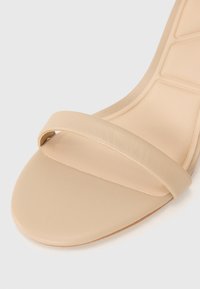 Nude nahka korkokenkä, jossa on tyylikäs siluetti, yksi hihna ja sileä, matta pinta pohjassa.