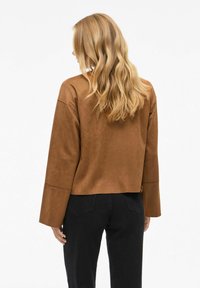 Haut court en suédine marron avec des manches longues, texture lisse, et pantalons noirs ajustés. Le haut présente un design minimaliste sans embellissements.