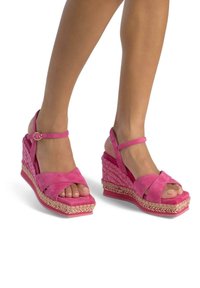 Sandales compensées en suède rose avec des brides entrecroisées, présentant une semelle en espadrille tissée et des détails en tresse décoratifs sur la semelle.