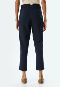 Marineblauwe op maat gemaakte broek met een hoge taille, een gladde textuur en een taps toelopende pijp. Zichtbare achterzakken en een ritsluiting.