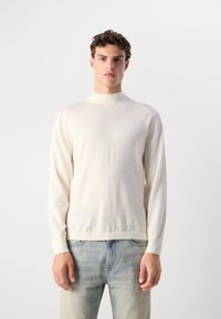 Maglione a collo alto cremoso, con maniche lunghe, realizzato in materiale morbido, caratterizzato da un design aderente e una discreta etichetta sul petto.