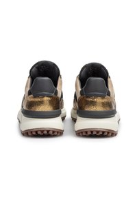 Ein Paar klobige Sneakers mit metallisch bronze texturiertem Absatz, beigen Wildlederseiten, schwarzen Lederelementen und dicken weißen Sohlen, von hinten betrachtet.