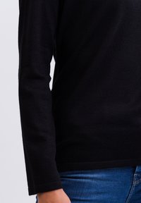 Schwarzes Langarmshirt aus einem weichen, strukturierten Material. Verfügt über einen runden Halsausschnitt und eng anliegende Bündchen, kombiniert mit blauen Jeans.