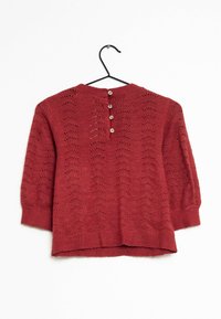 Pull en tricot rouge avec un motif de vagues, manches trois-quarts, et cinq petits boutons à l'arrière, suspendu sur un cintre noir.