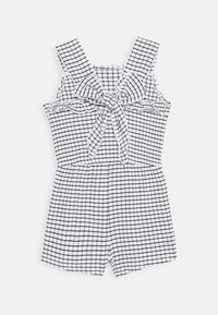 Mono de cuadros en blanco y negro con tirantes rizados y un detalle de lazo en la parte delantera. Hecho de una tela ligera, cuenta con un top ajustado y pantalones cortos holgados.