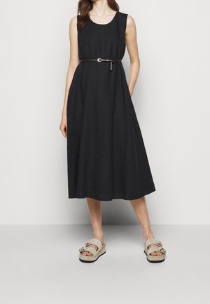 Mujer con vestido midi negro sin mangas con un cinturón fino marrón y sandalias de plataforma beige con hebillas doradas.