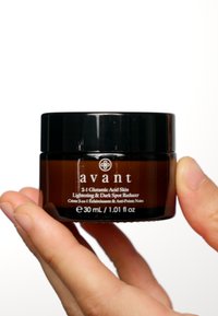 Tarro de vidrio marrón con tapa negra, etiquetado "avant 2-1 Ácido Glutámico Aclarante de Piel y Reductor de Manchas Oscuras", 30 mL, sostenido en una mano.