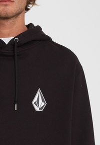 Felpa nera con cappuccio e cordino, caratterizzata da un grande logo a forma di diamante bianco sul petto. Tessuto morbido con vestibilità rilassata e tasca a marsupio.