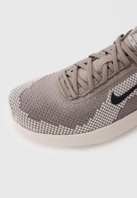 Lys grå sneaker med tekstureret strikoverdel, der har et sort Nike swoosh, flade snørebånd og en polstret hvid sål med et mønstret finish.