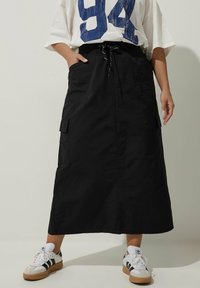 Svart cargokjol med dragsko i midjan, sidofickor och rak silhuett. Kombinerad med vita sneakers med svarta ränder.